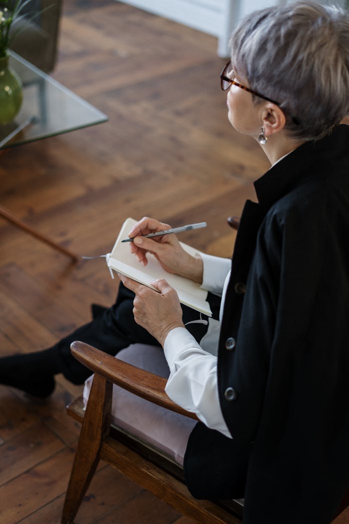 A professional woman with glasses taking notes while seated indoors, depicting consultation or therapy.